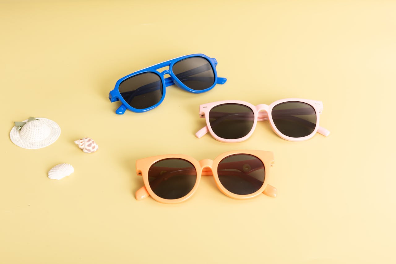 gallery-02 A flat lay of three colorful sunglasses on a yellow background with beach accessories. Ideal for summer and fashion themes.